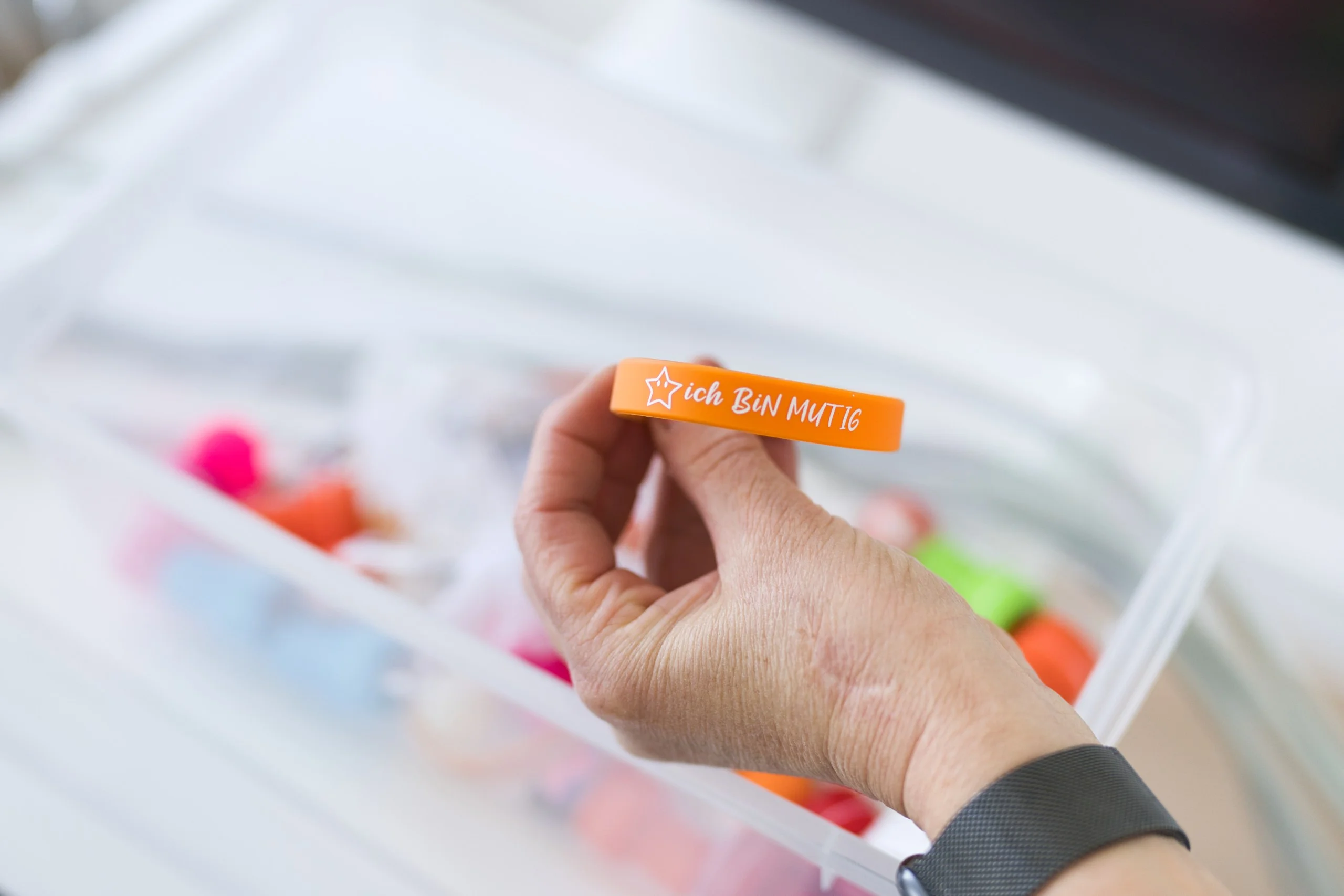 Kinder- & Jugendprophylaxe in Schwäbisch Gmünd: Einfühlsame Zahnvorsorge Hand hält ein orangefarbenes Mutmach-Armband mit der Aufschrift "ich bin mutig"
